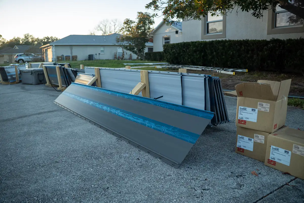 Grey standing seam panels staged on wooden cradles in the driveway with the protective film still on