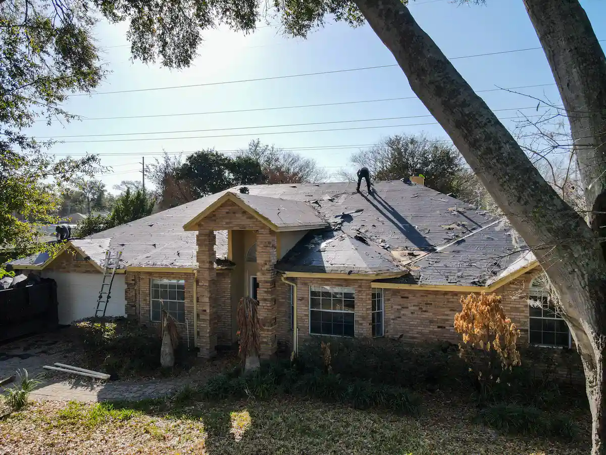 The Orlando home from the front right during tear-off, with a roofer up on the ridge