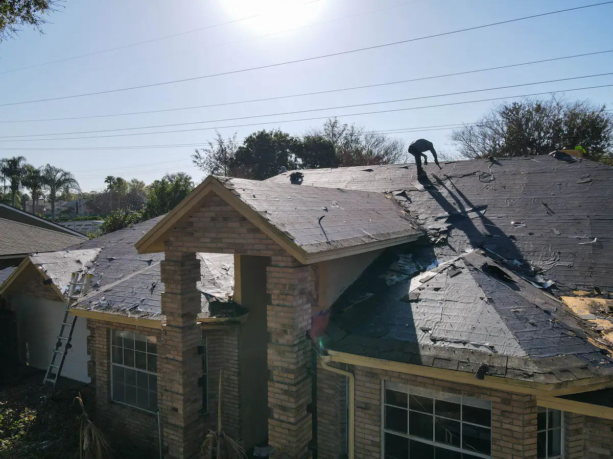 The Orlando home mid tear-off, with a roofer working the far slope in low afternoon sun