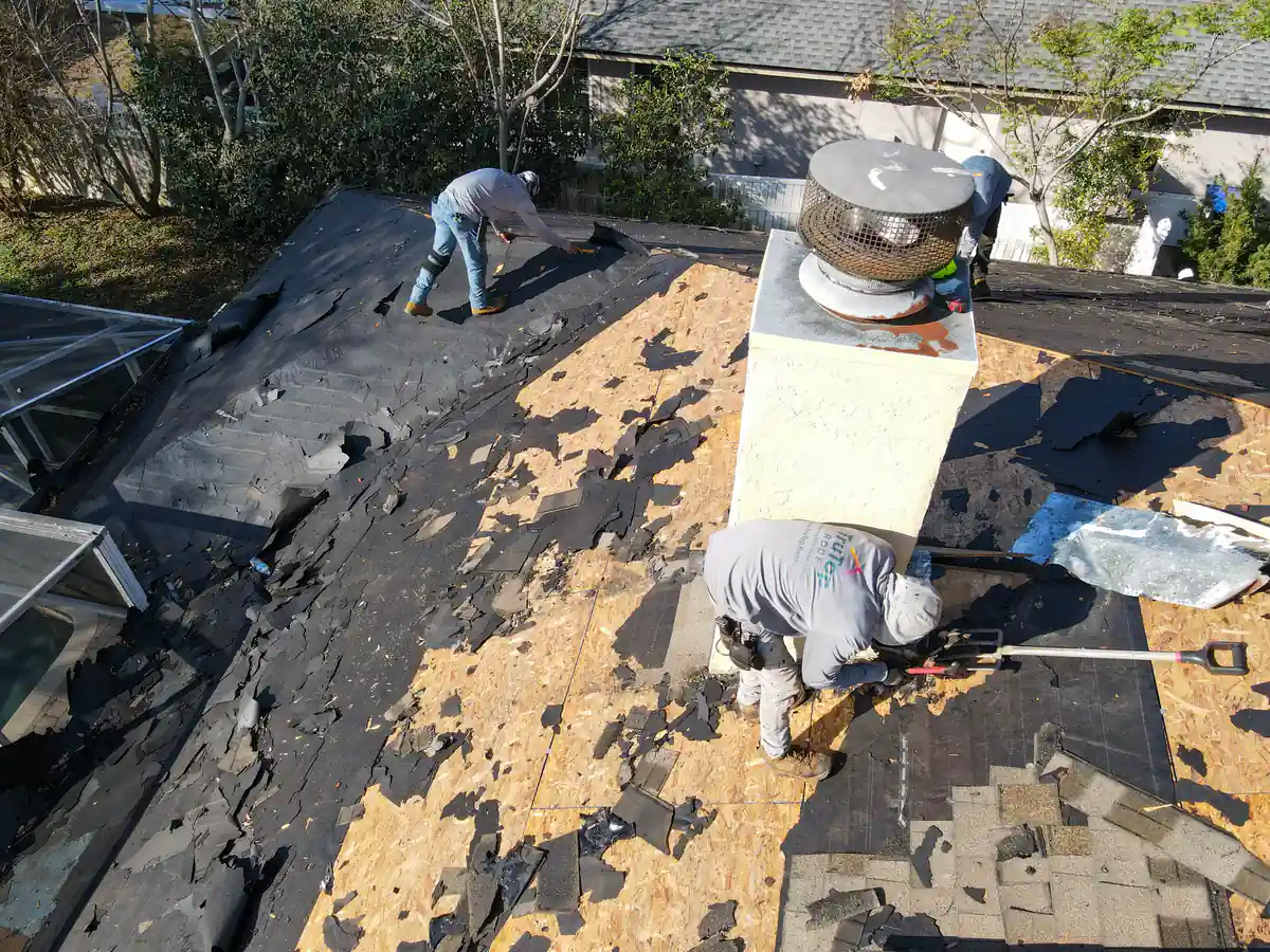 Two roofers clearing old shingles beside the chimney on the Orlando home