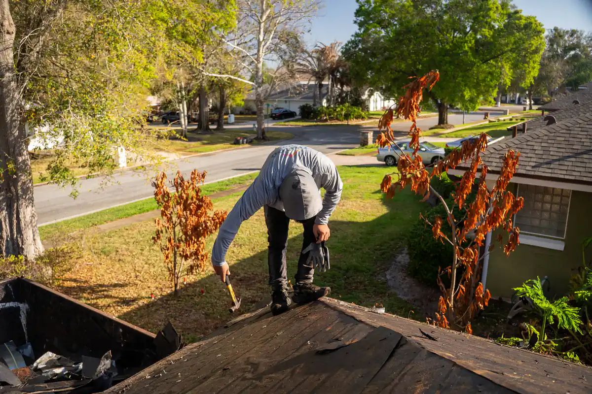 Roofer prying up old shingles at the front edge of the Orlando roof